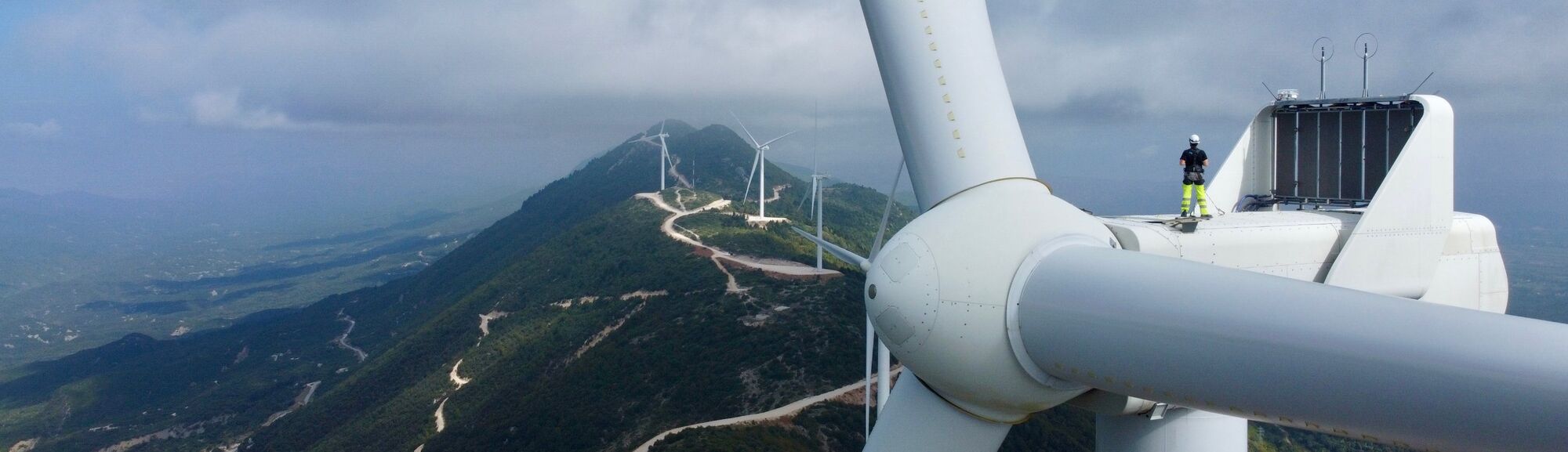 Technician standing on a wind turbine nacelle above a mountain-ridge wind farm